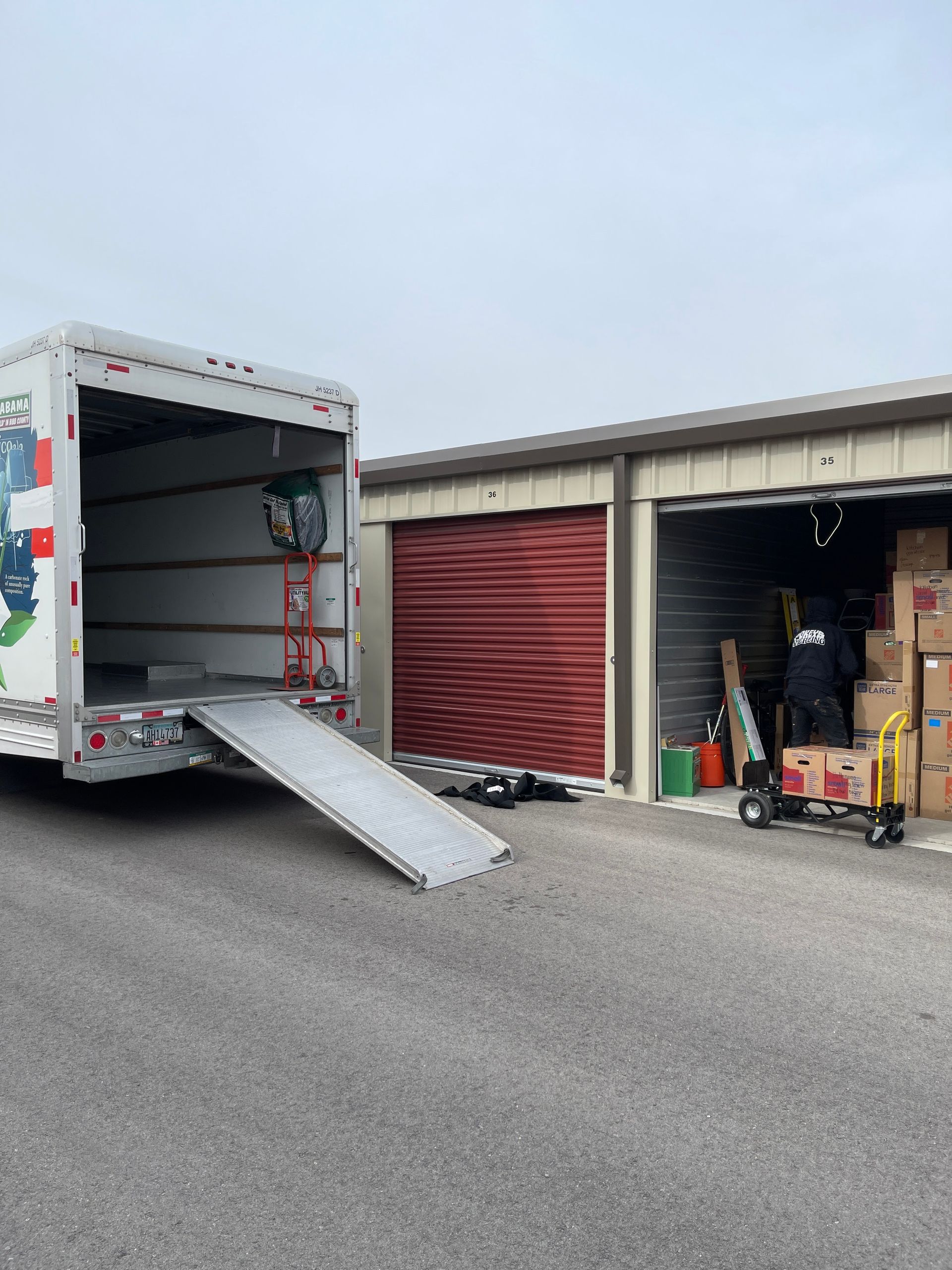 Moving truck with ramp open, loading items into storage units.