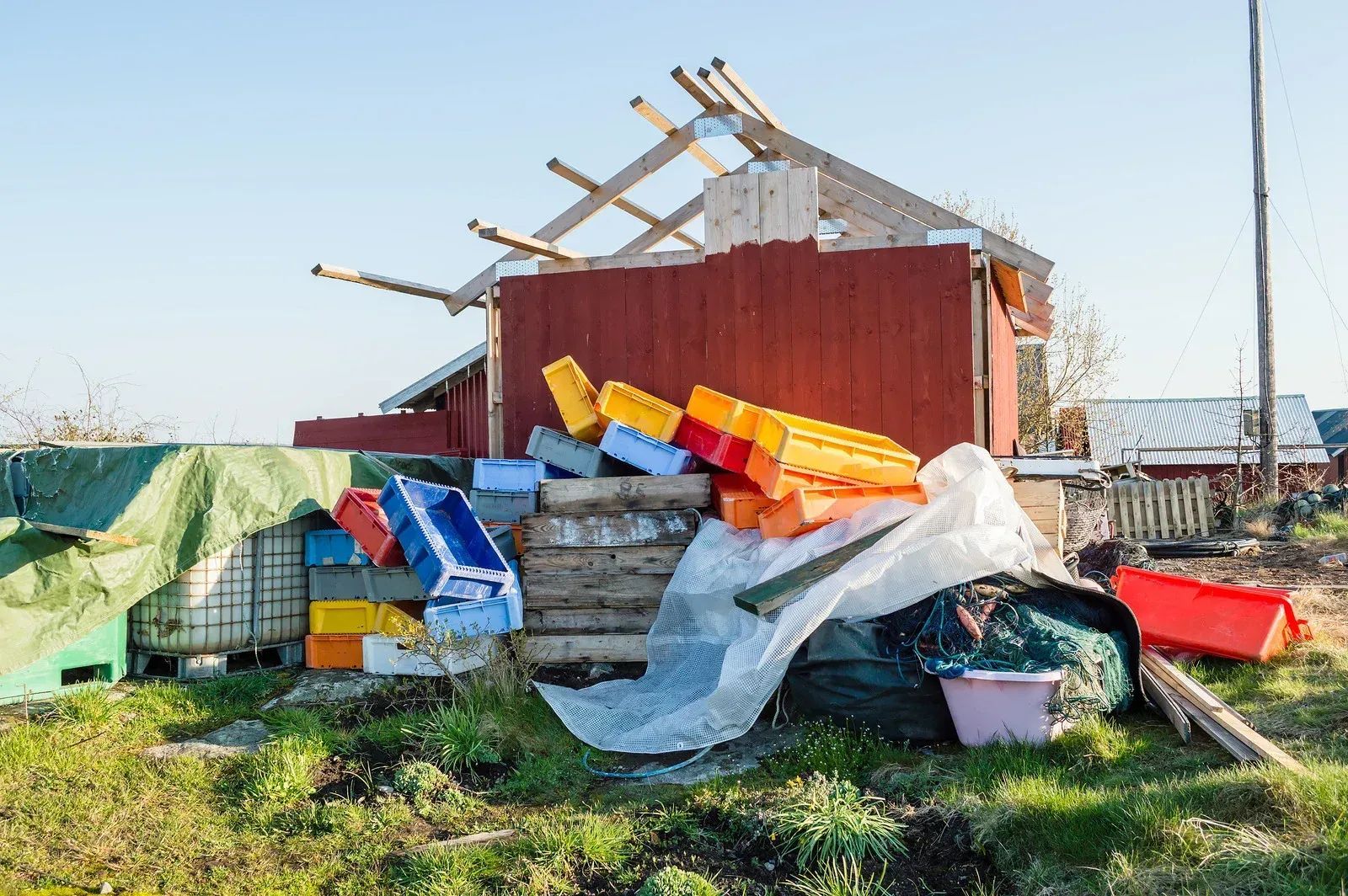 Collapsed debris and colorful bins piled in a grassy yard beside a damaged red building