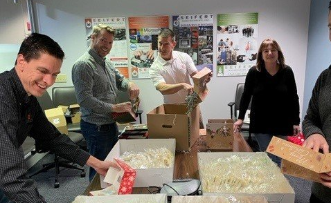 Seifert employees around a table, assembling cookie boxes out of cardboard.