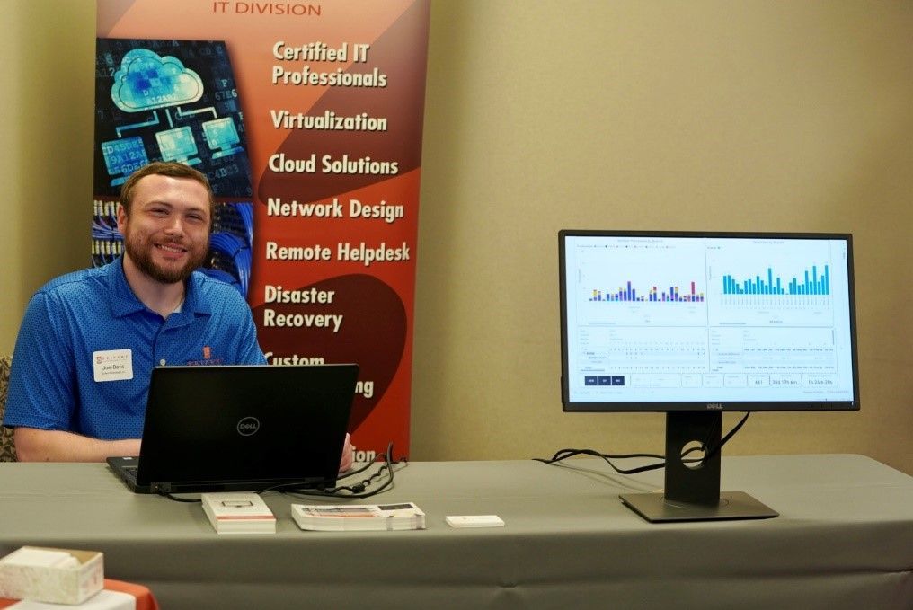 A Seifert employee attending an info table. A monitor with reports charts is visible.