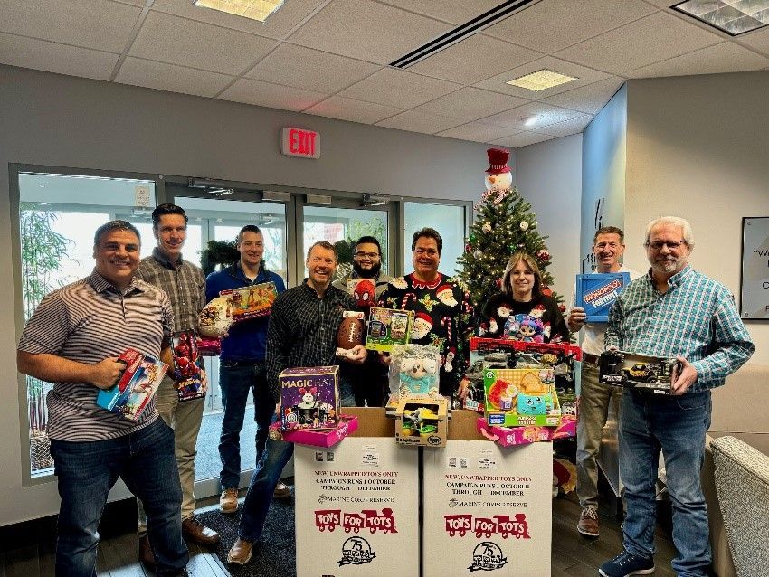 Seifert employees holding new toys, next to two Toys for Tots boxes.