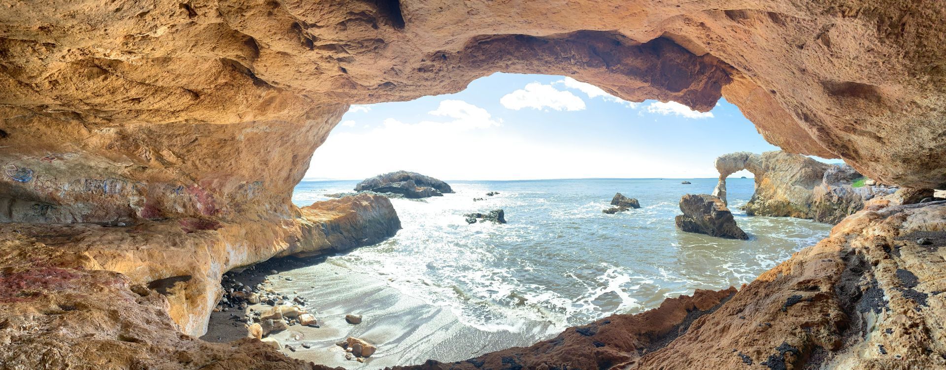 Rocky sea cave opening to bright ocean waves and distant cliffs