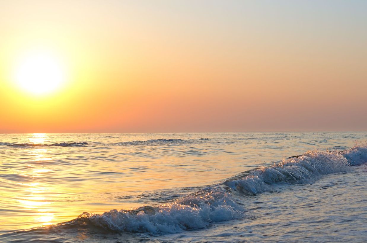 Sunset over a calm ocean with golden light and gentle waves rolling to shore