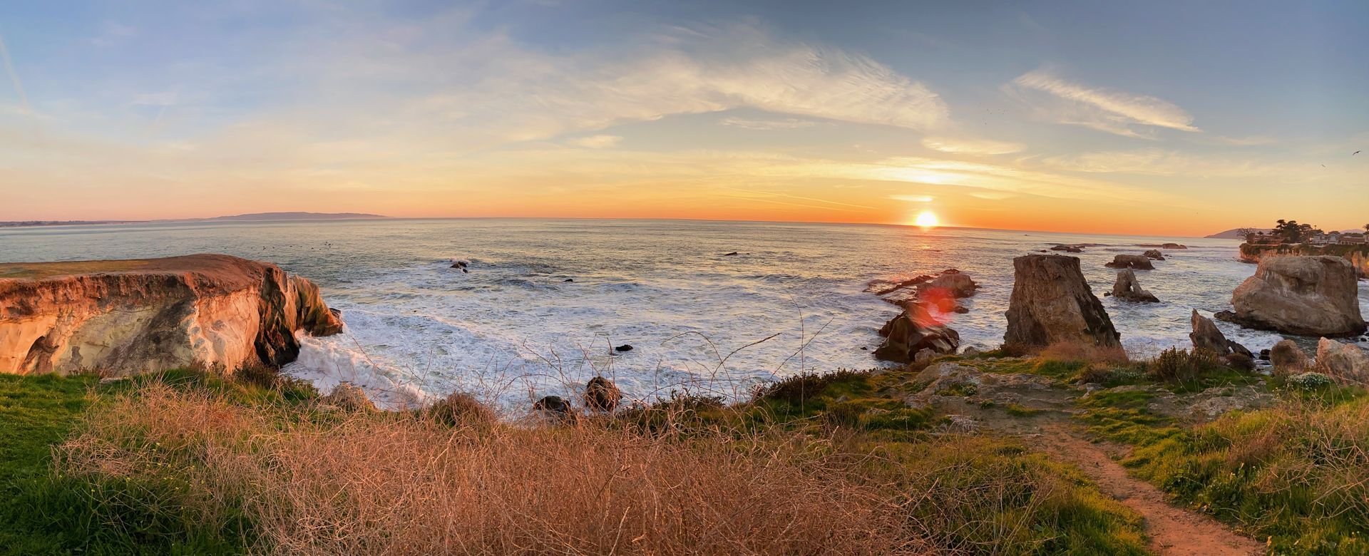 Sunset over rocky sea cliffs with waves and a grassy foreground