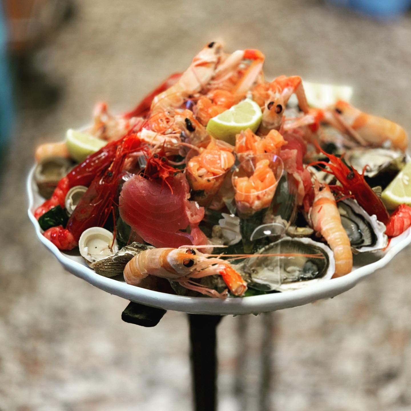 Piatto di frutti di mare con aragosta, gamberi, cozze e spicchi di lime su un piatto rialzato.