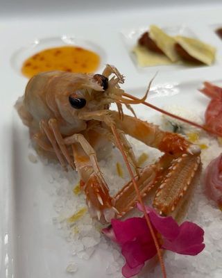 Gamberi cotti su un piatto bianco con salsa, spicchi di limone e guarnizione.