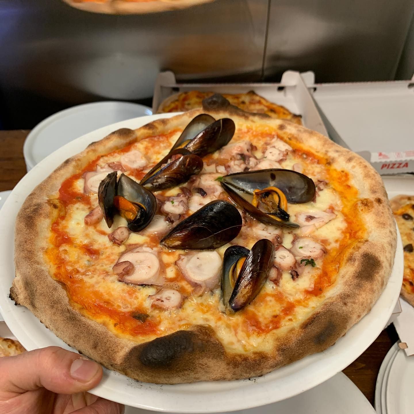 Piatto monoporzione con una pizza ai frutti di mare guarnita con cozze, nella cucina di un ristorante.