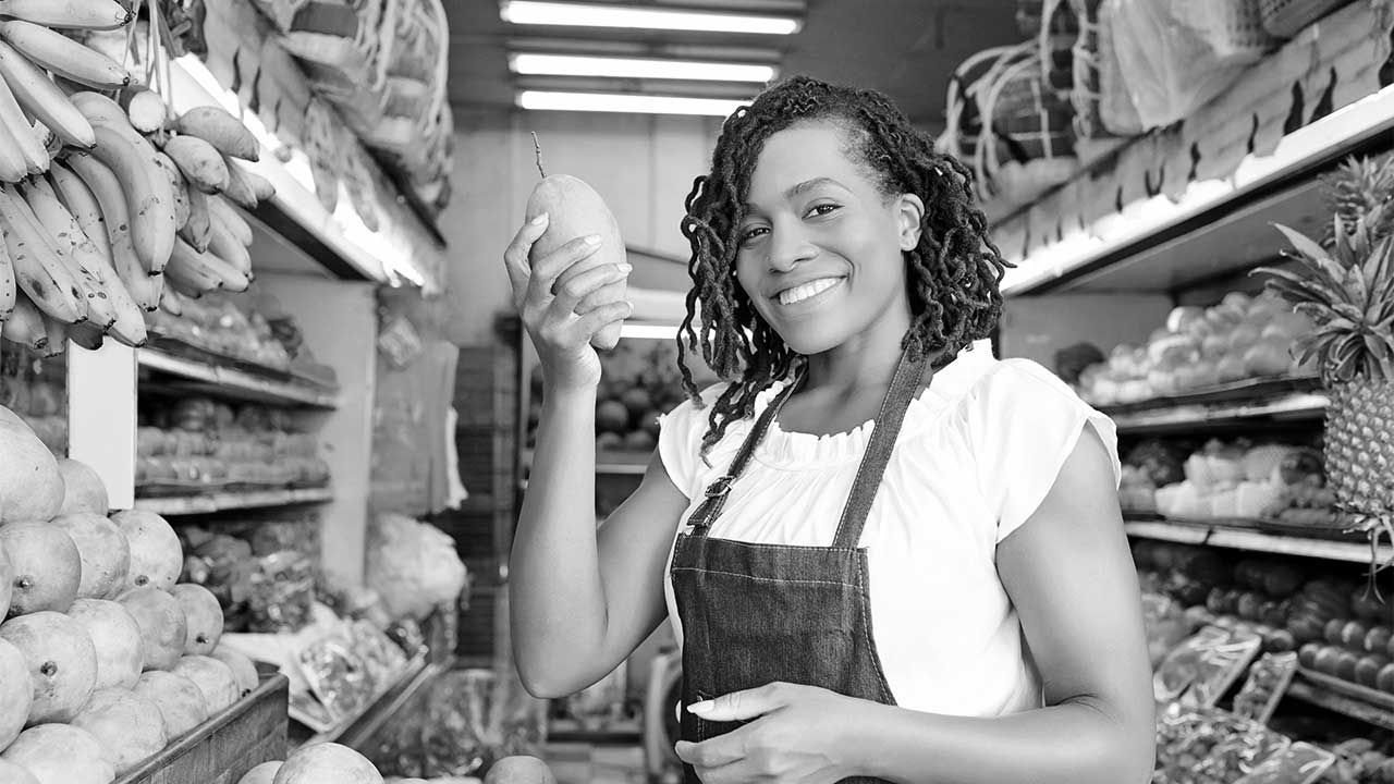 A woman in an apron is standing in a grocery store.