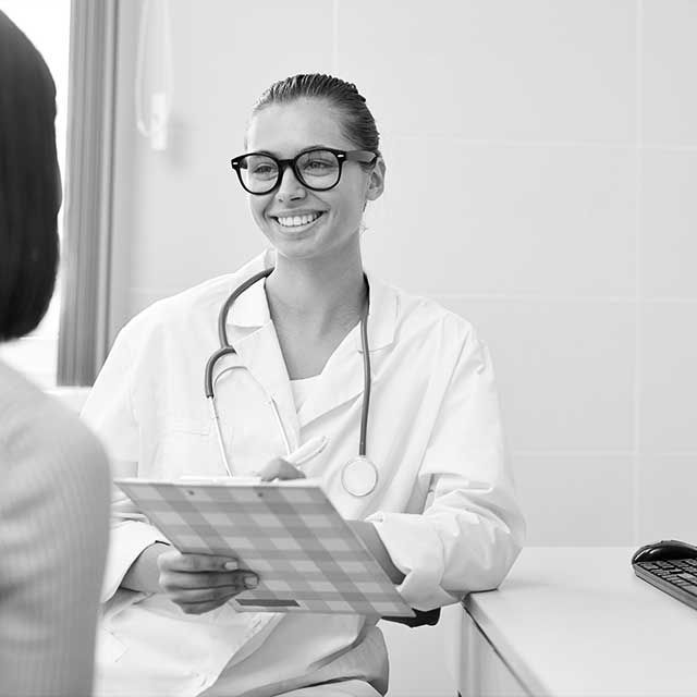 A doctor is smiling while talking to a patient in a black and white photo.