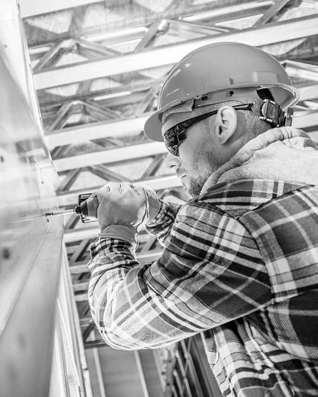 A black and white photo of a construction worker wearing a hard hat and safety glasses.