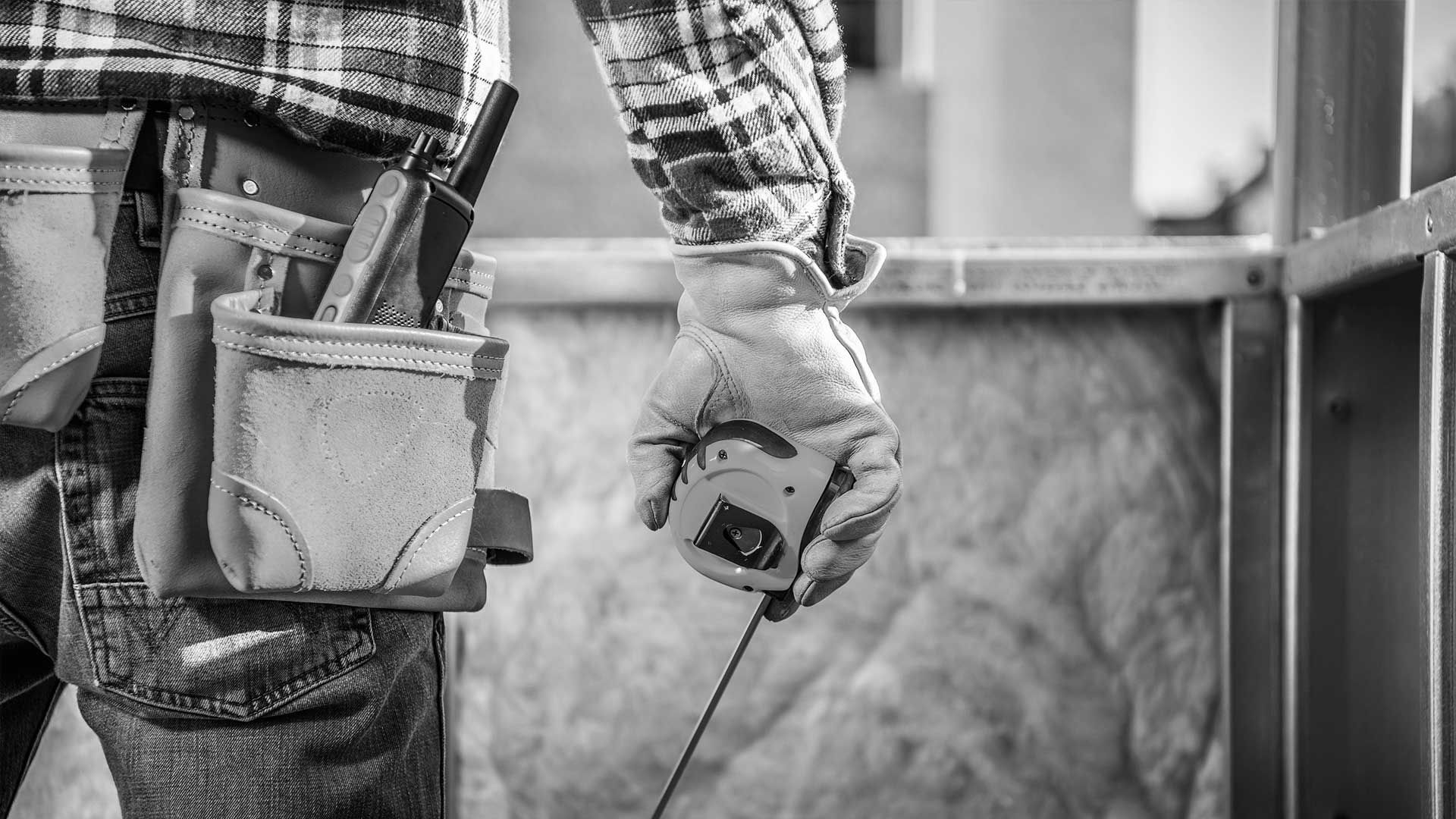 A black and white photo of a construction worker holding a tape measure.