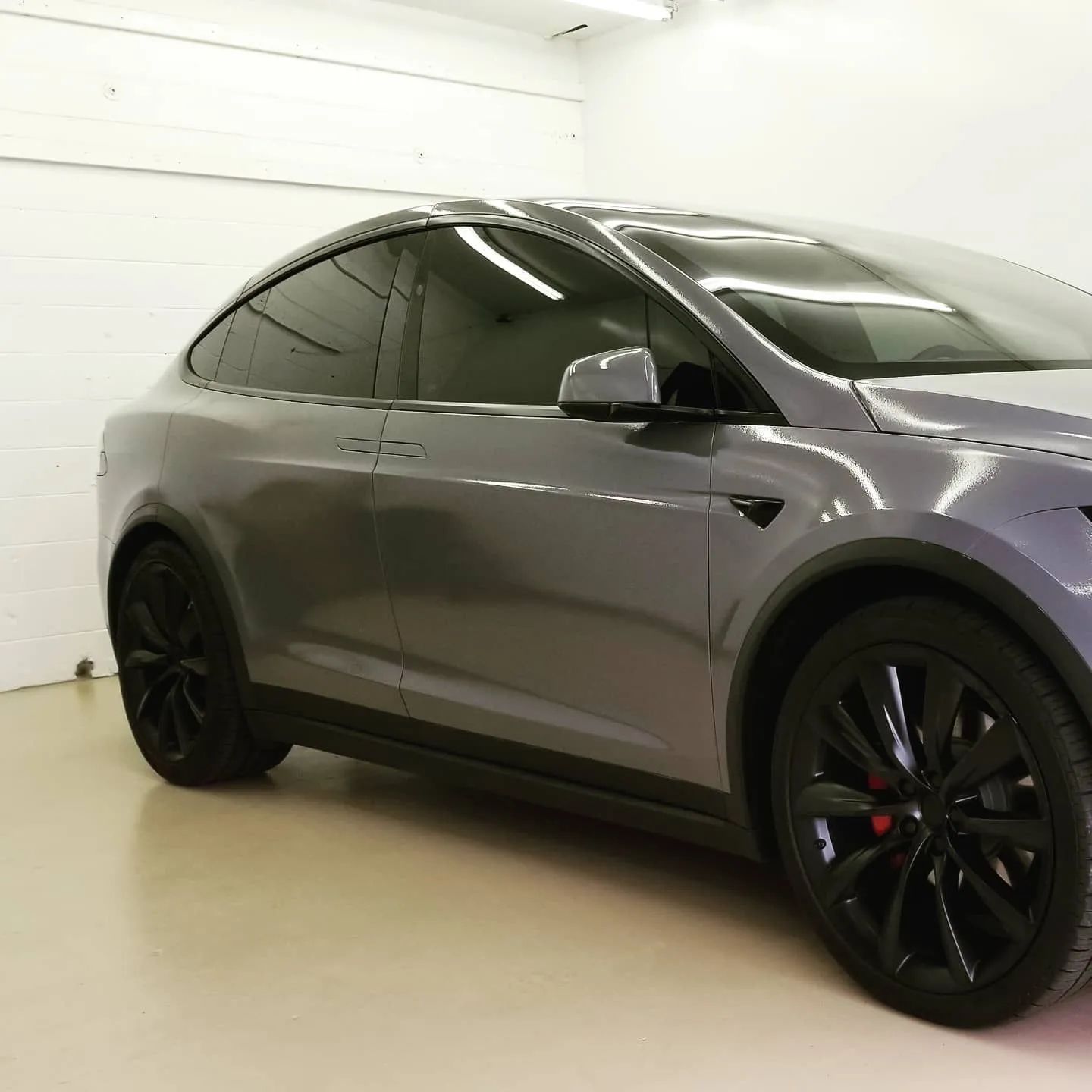 Gray Tesla SUV parked indoors with black wheels and tinted windows
