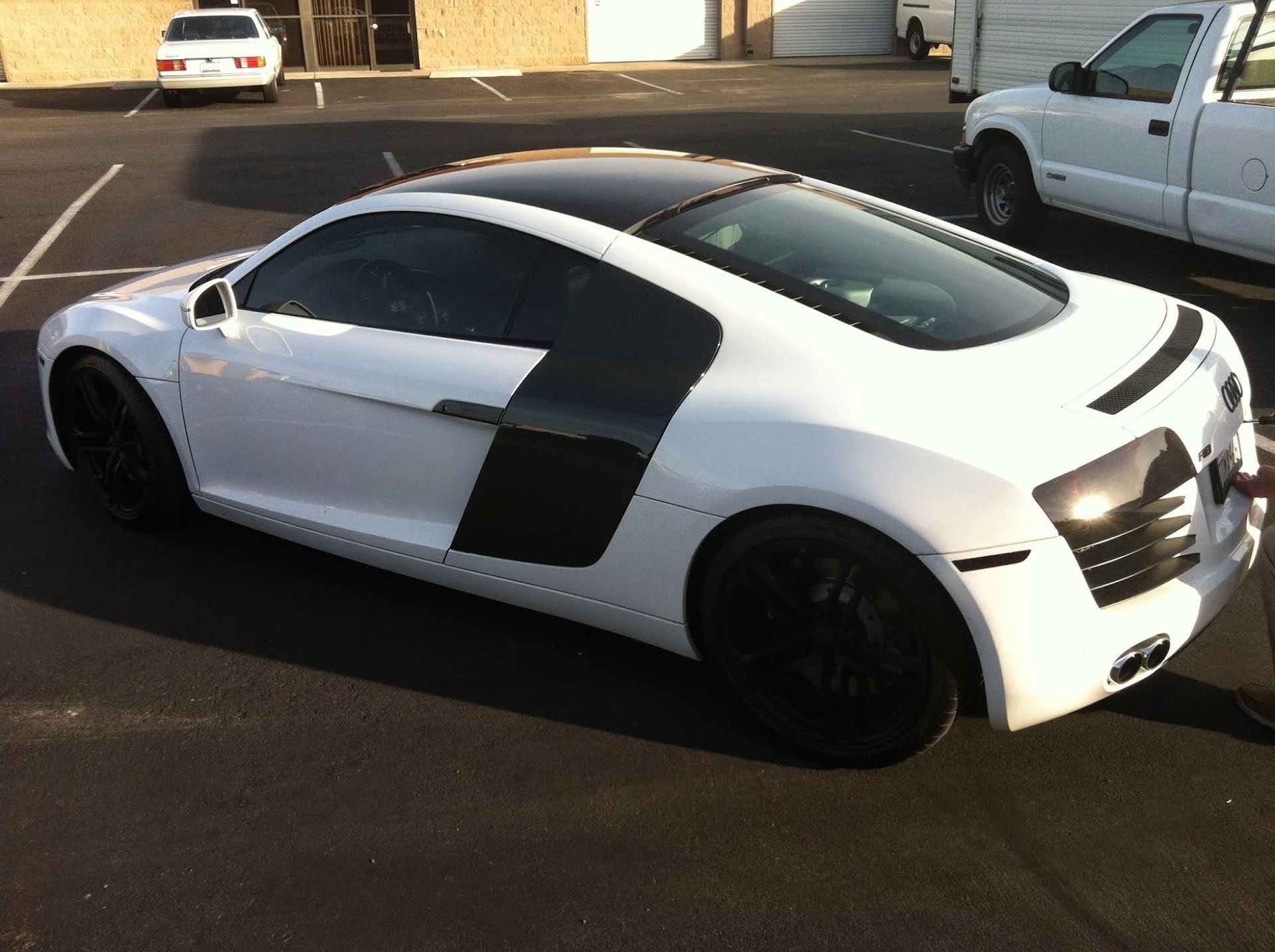 White Audi R8 coupe with black accents and wheels parked on asphalt in front of a building.