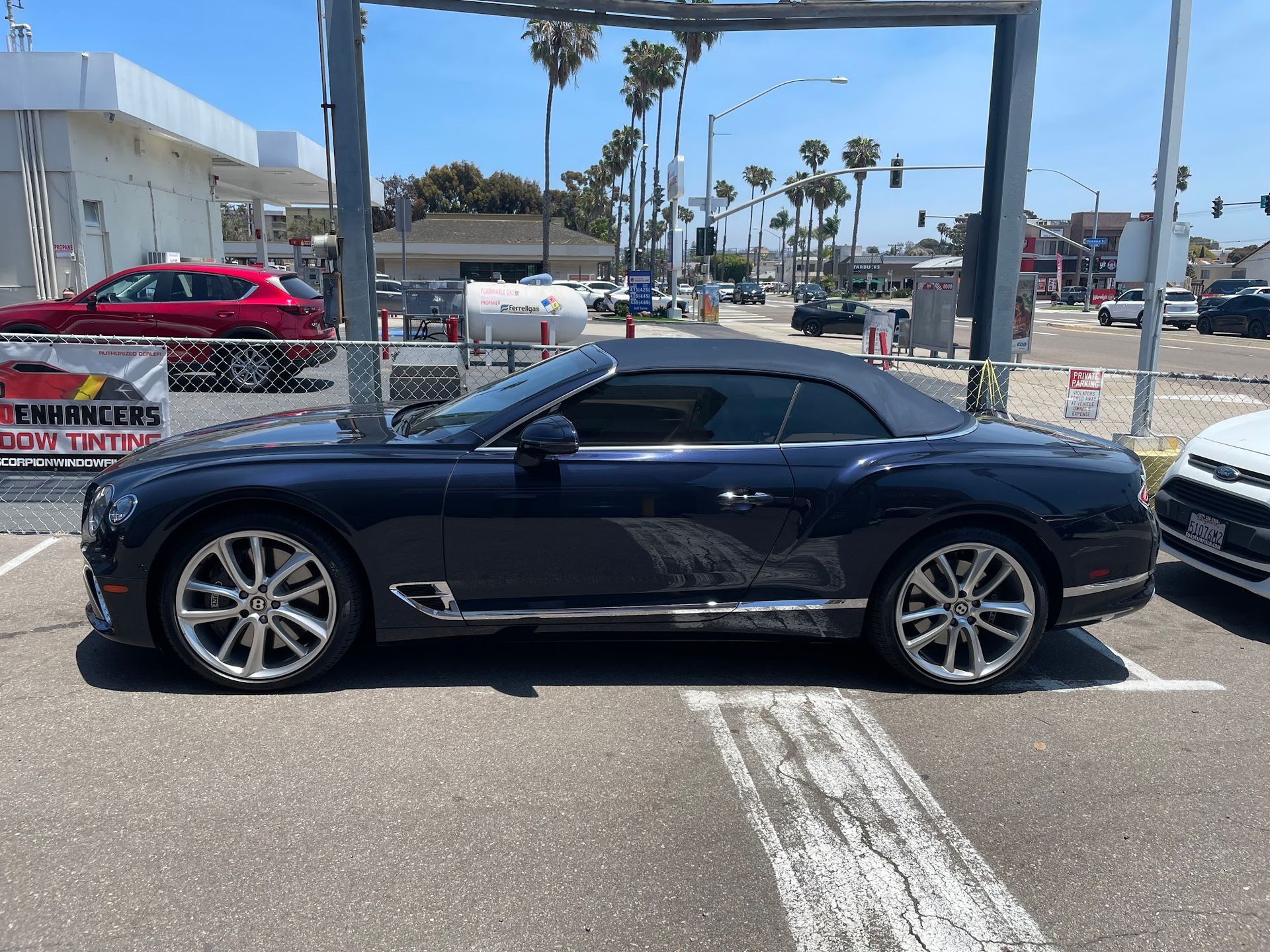 Dark blue Bentley convertible parked near a business with a white canopy in a sunny setting.