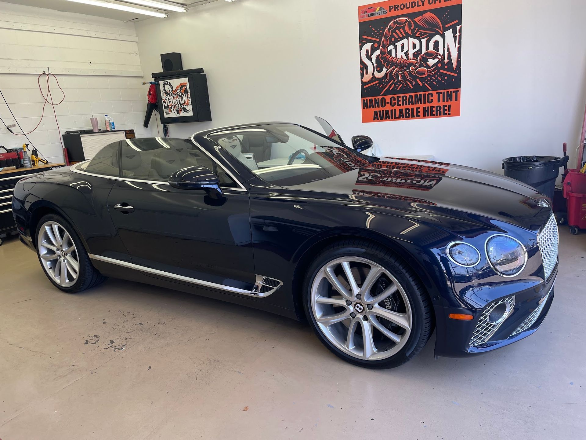 Dark blue Bentley convertible in a garage with a poster.