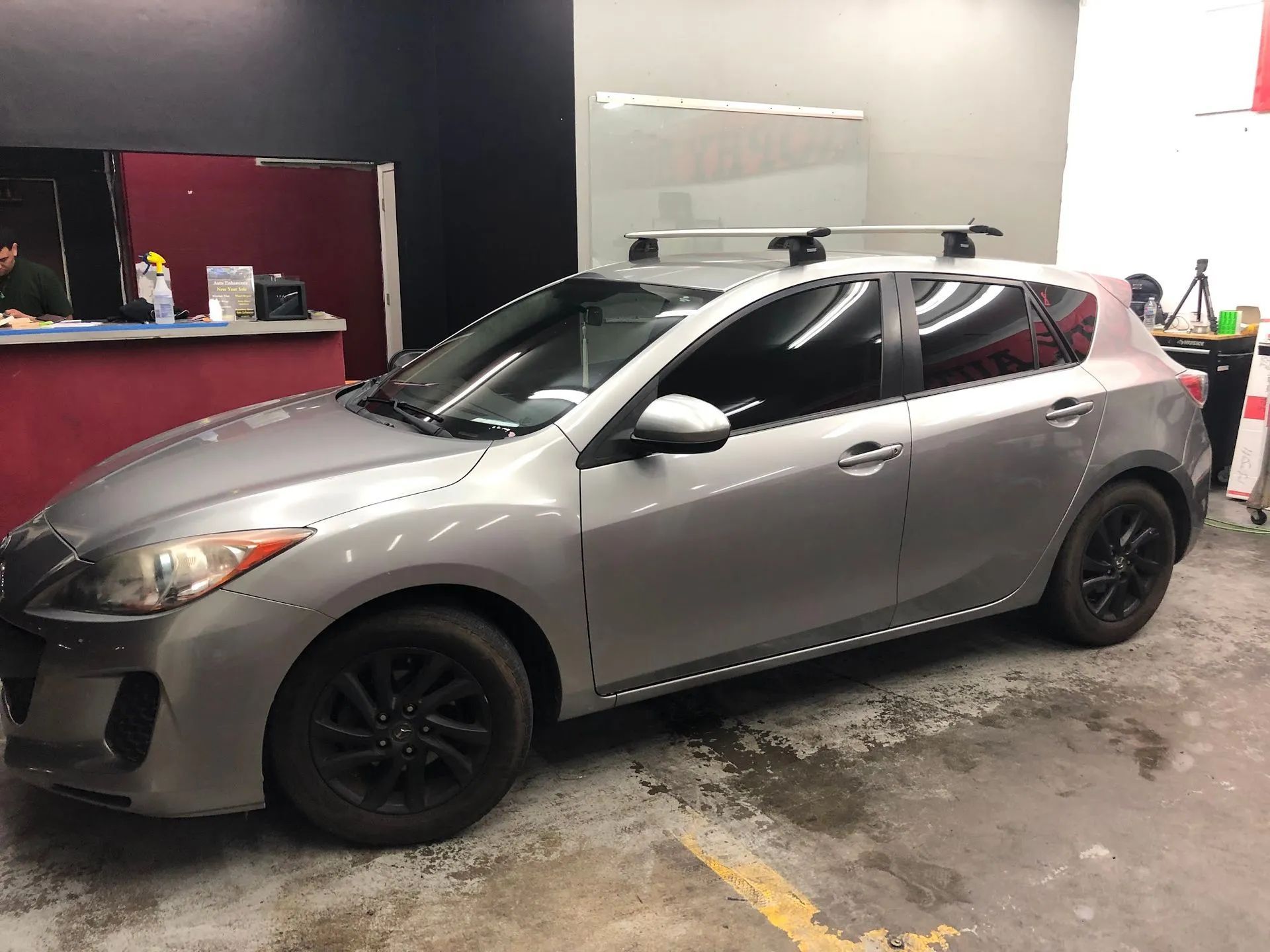 Silver hatchback car in a garage, parked on a wet concrete floor with black rims.