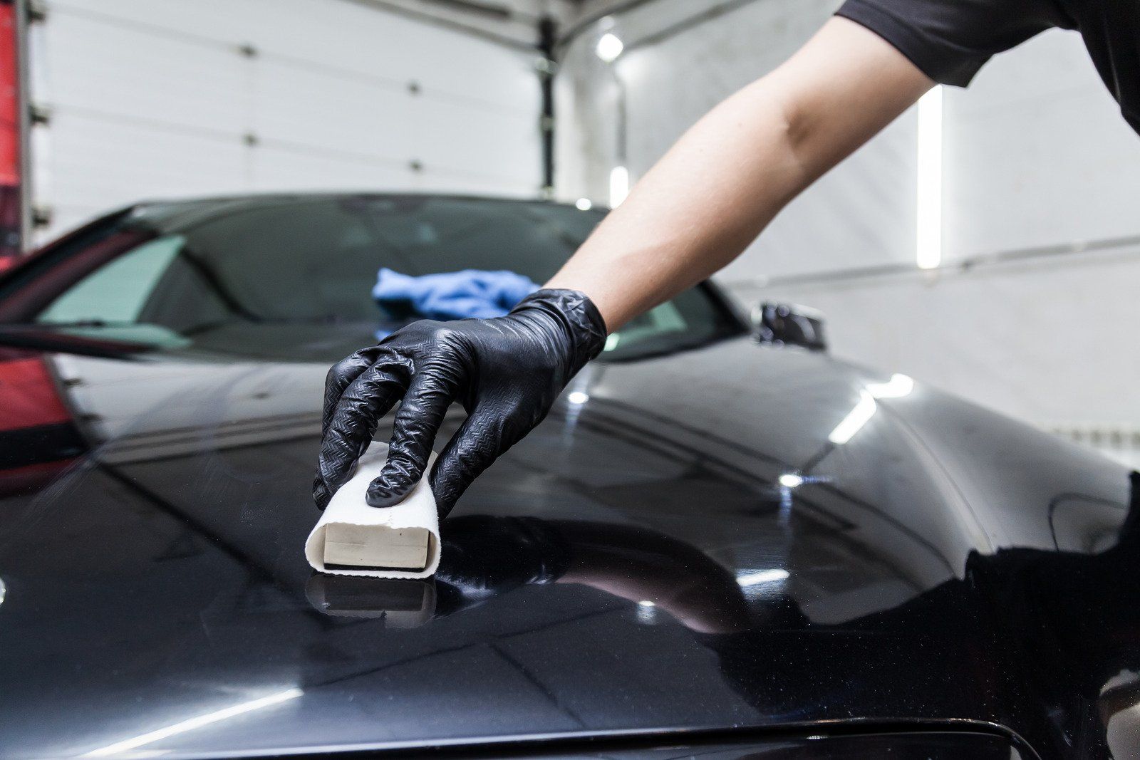 Gloved hand polishing a black car hood in a garage