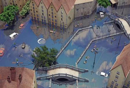 An aerial view of a flooded city street with submerged cars, surrounded by buildings, trees, and bridges.