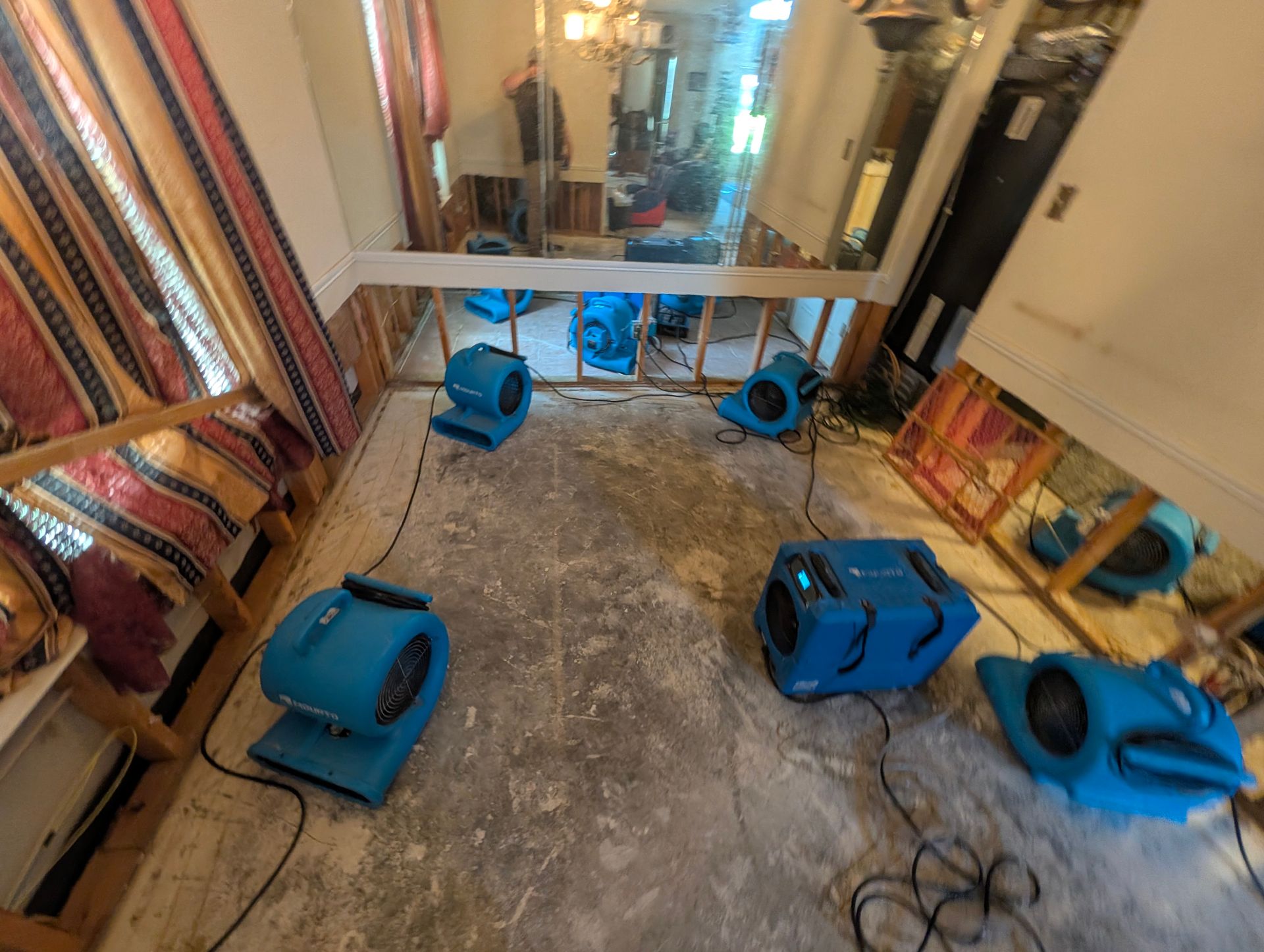 Blue industrial fans on a tiled floor in a small room with exposed walls and construction materials.