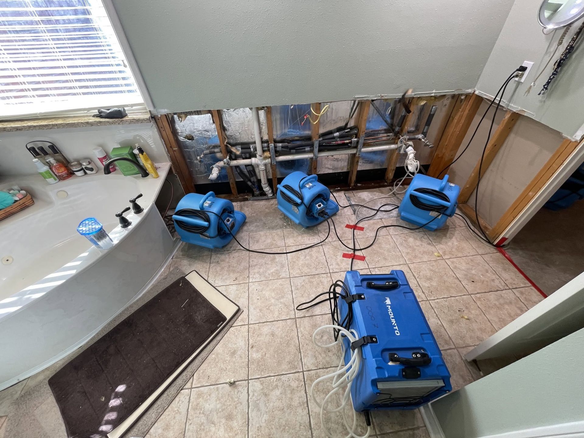Blue industrial fans on a tiled floor in a small room with exposed walls and construction materials.