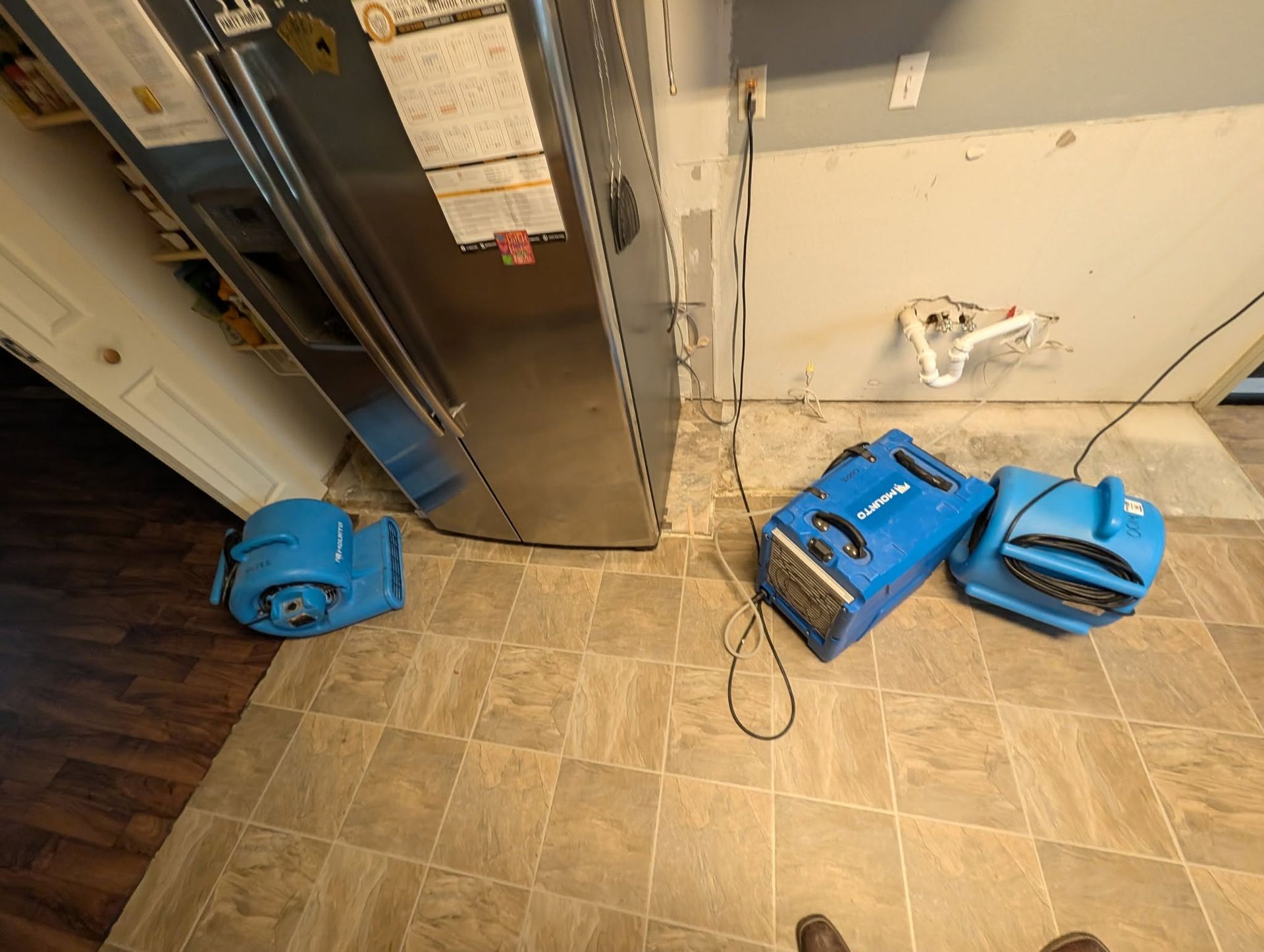 Three blue cleaning machines on a tiled floor beside a stainless steel cabinet and wall outlet.