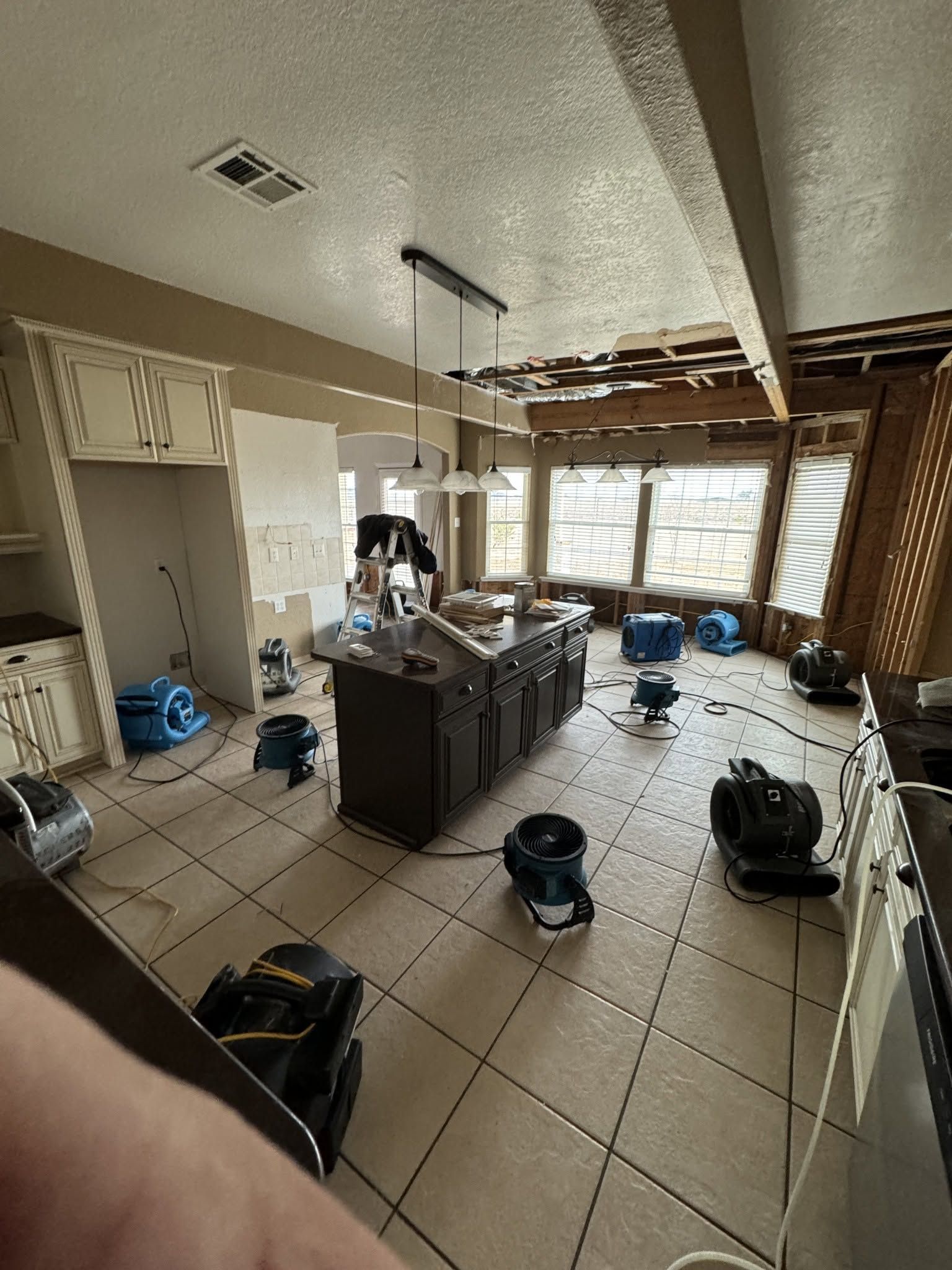 Damaged kitchen with broken ceiling, scattered debris, and cleaning equipment on tiled floor