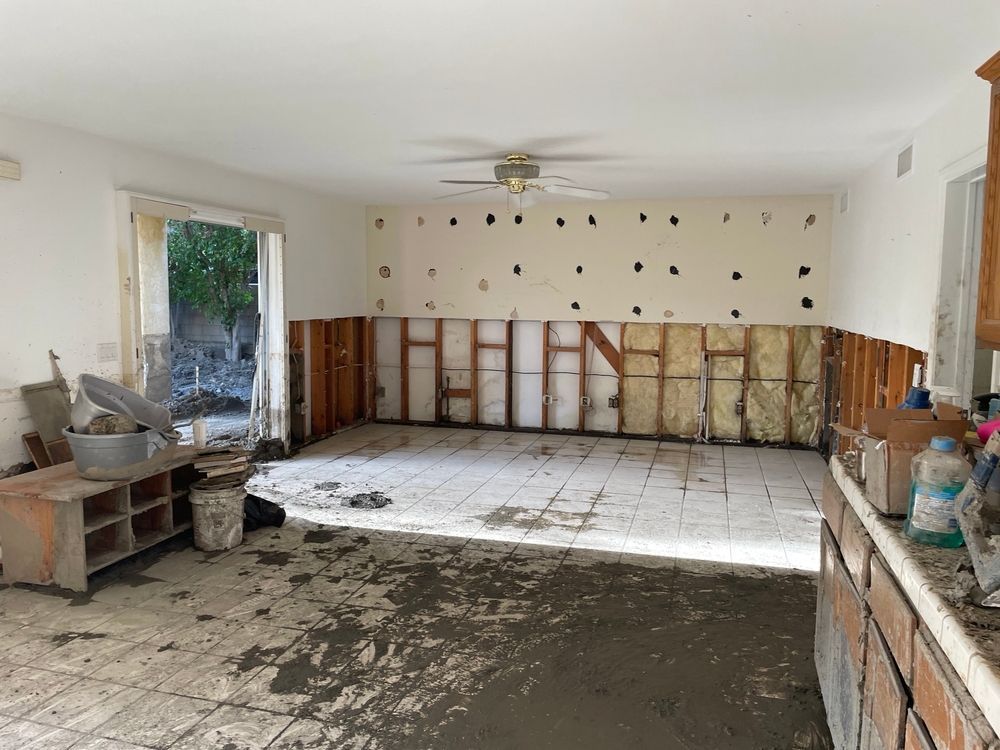 Damaged living room with exposed walls, torn flooring, and debris during renovation