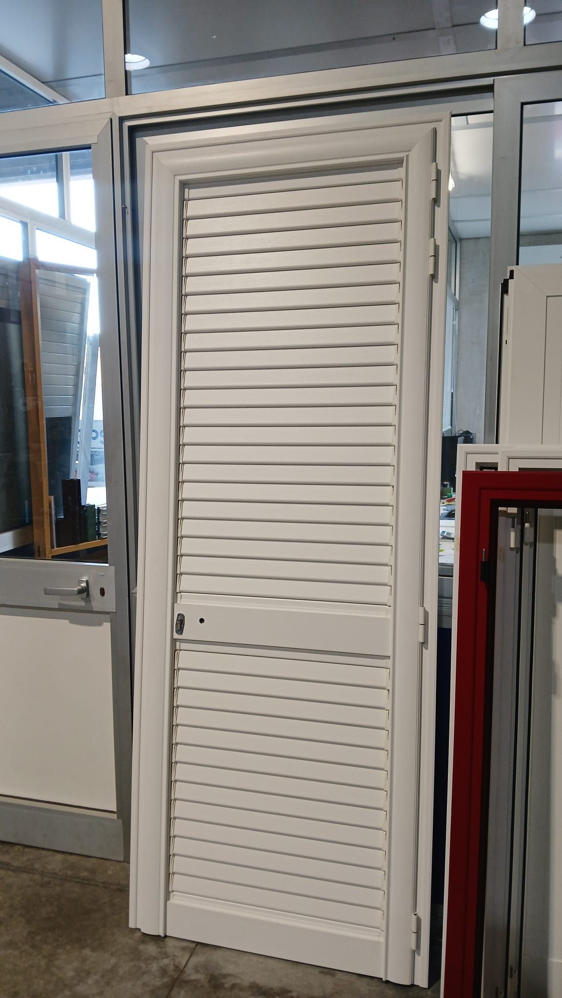 Porta a persiana bianca in un interno in stile industriale con telaio in metallo e pannelli in vetro.