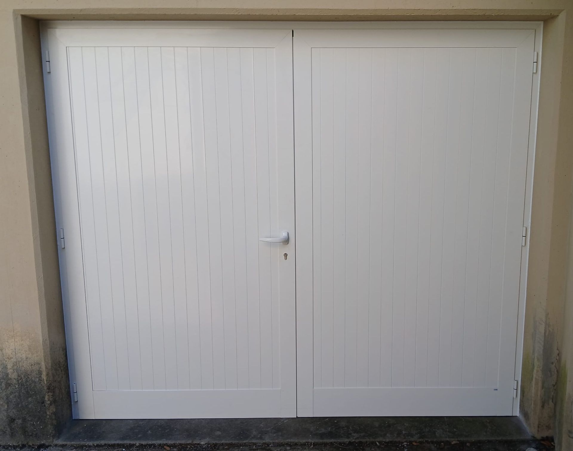 Doppia porta da garage bianca con maniglia piccola, incastonata in una parete beige.
