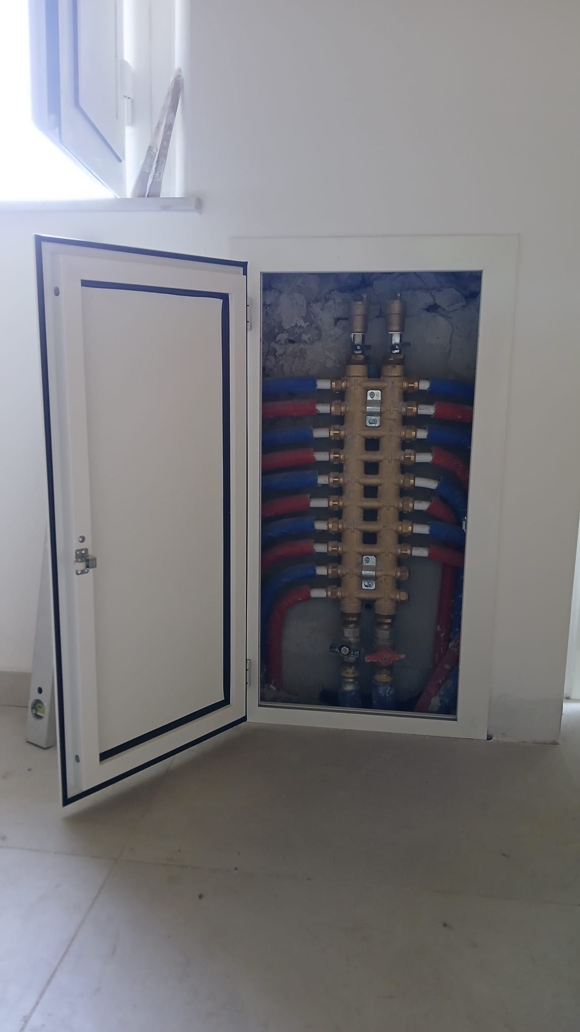 Quadro elettrico aperto con fili a vista e cavi colorati in un locale di servizio bianco.