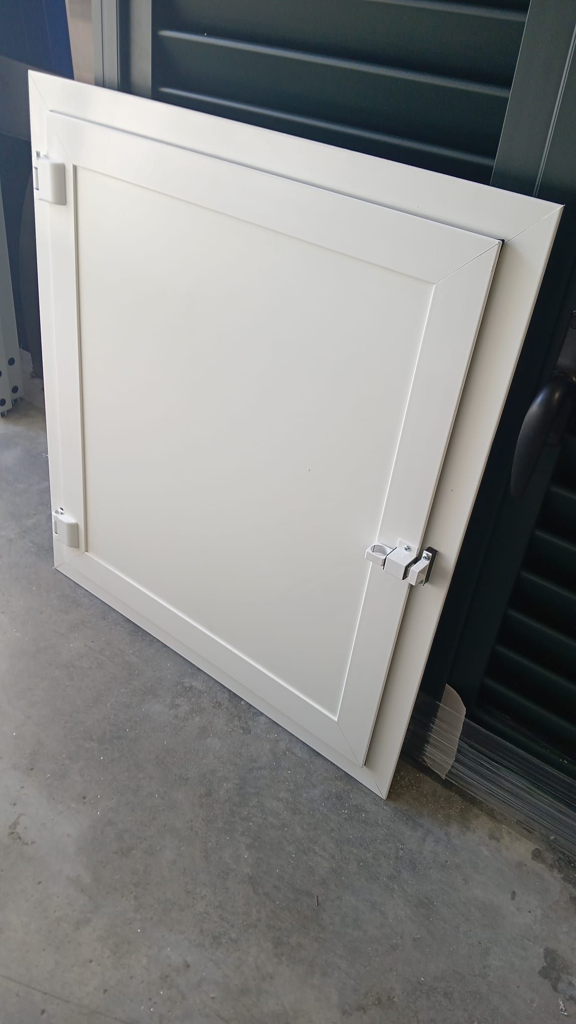 Pannello bianco di un'anta di un armadio appoggiato a una parete in un garage, con un chiavistello metallico sul lato destro.