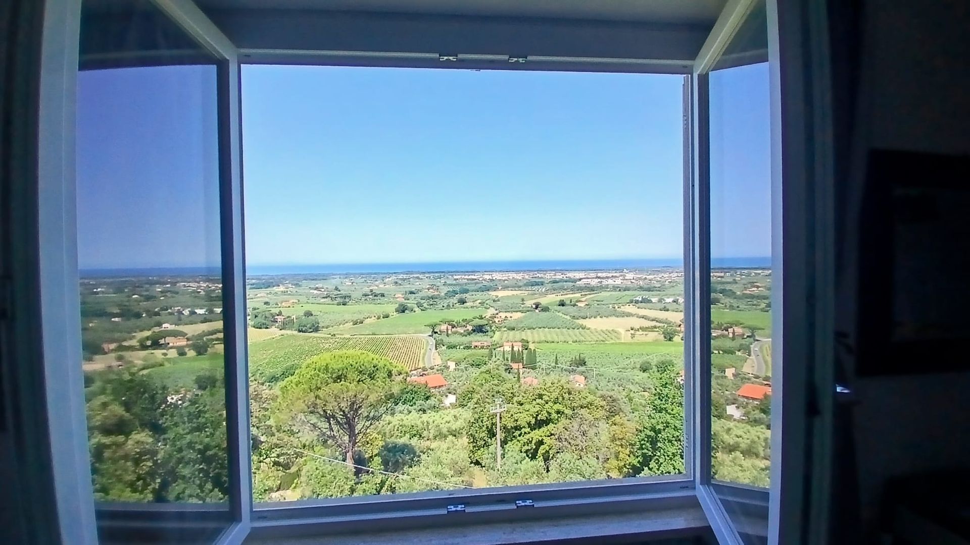 Finestra aperta che incornicia una campagna verdeggiante sotto un cielo azzurro