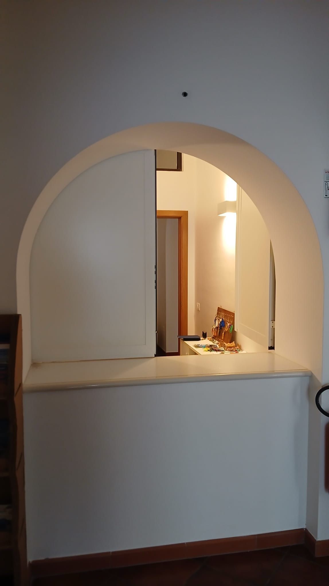 Corridoio interno con un'ampia apertura ad arco che conduce a una stanza illuminata al di là.