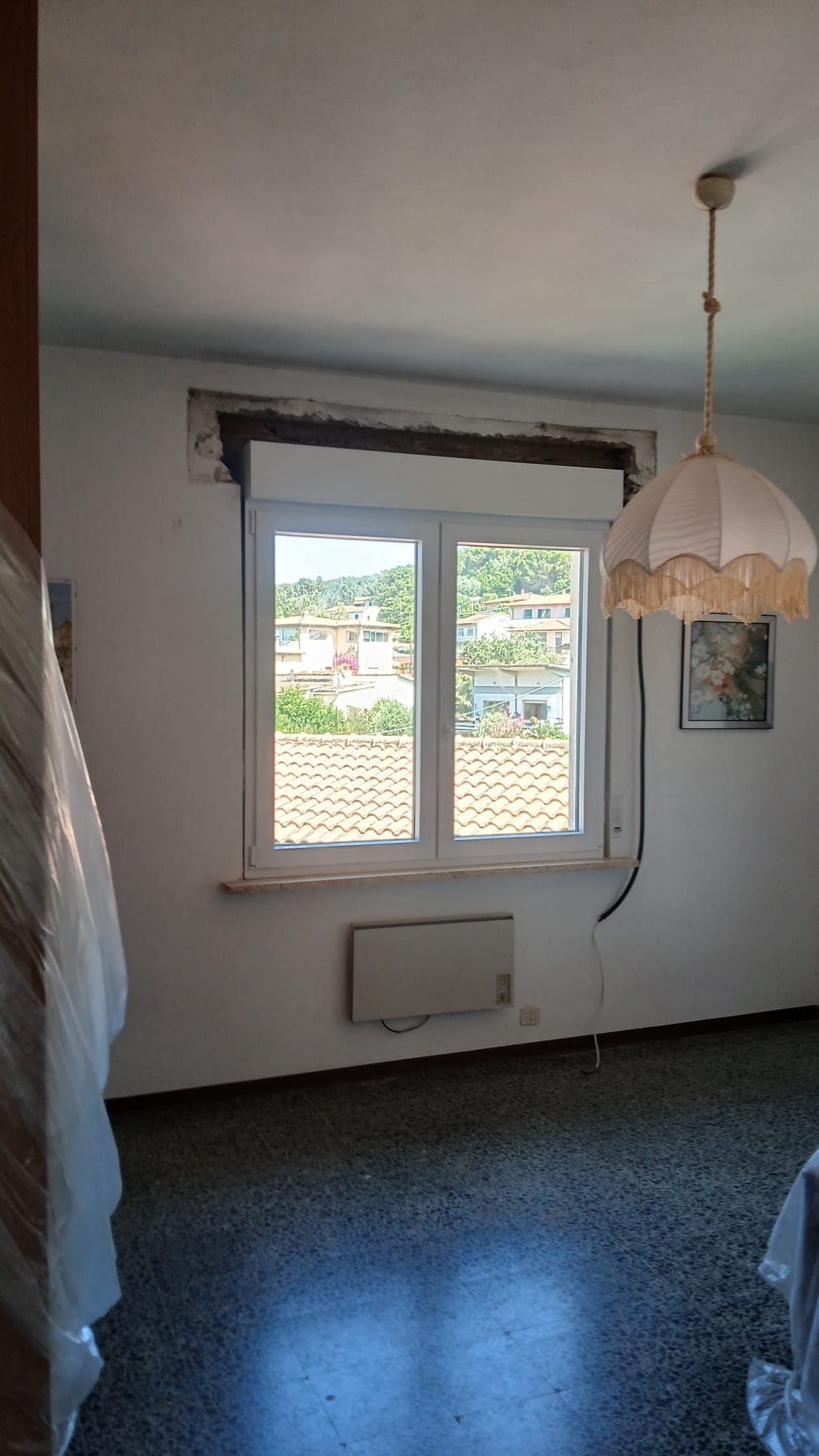 Una stanza buia e vuota con una finestra, una lampada a sospensione e pareti consumate, vista dall'interno.