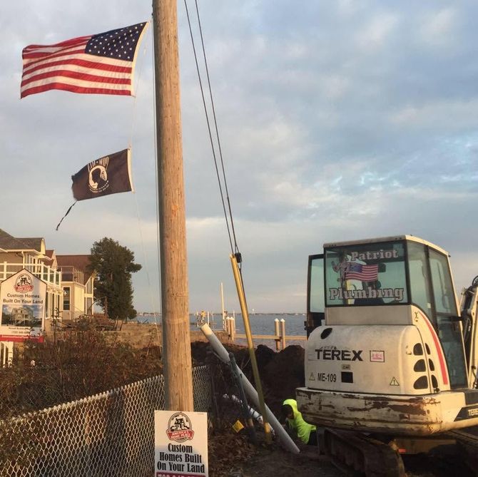 Flags waving beside a Terex excavator at a coastal construction site at sunset