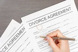A hand holds a pen over a divorce agreement document resting on a wooden surface.