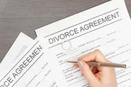 A hand holds a pen over a divorce agreement document resting on a wooden surface.