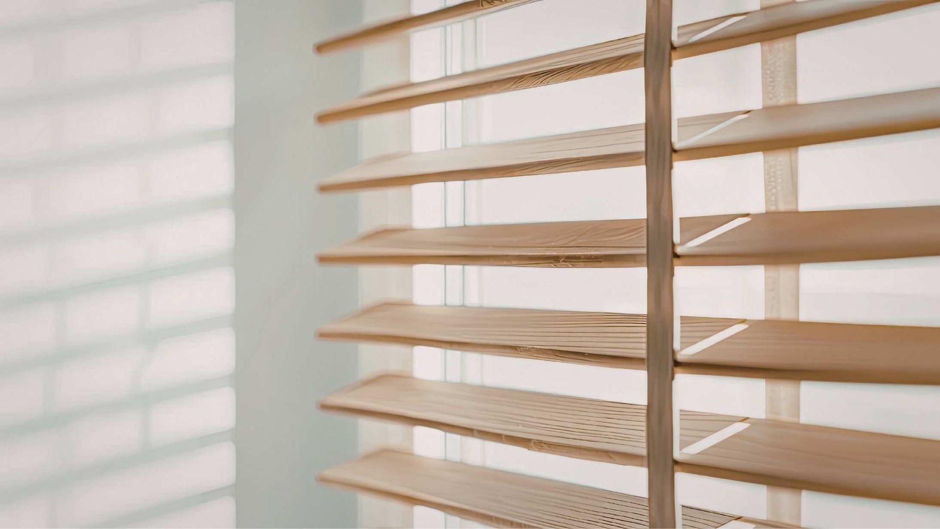 Wooden blinds, partially open, casting a shadow on a light blue wall.
