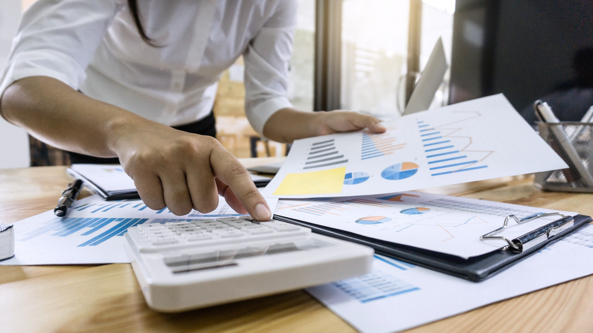 Person using a calculator, looking at charts with graphs and data in an office setting.
