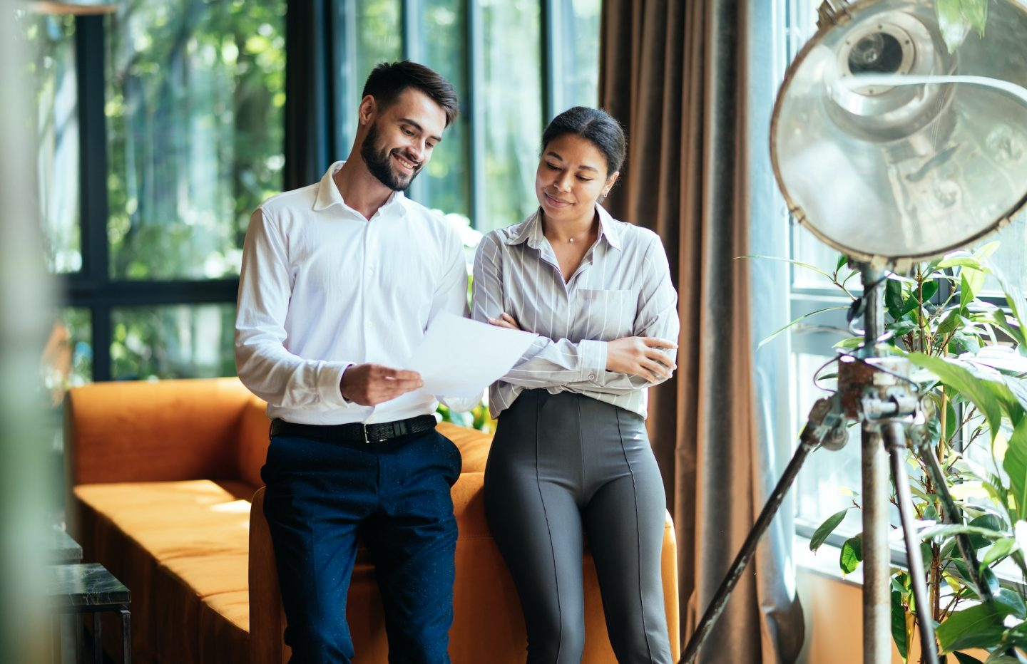 Man and woman reviewing papers near a window with sunlight and indoor plants.