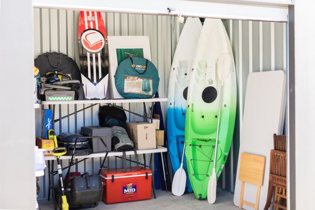 A self storage shed filled with kayaks , surfboards , and other items.
