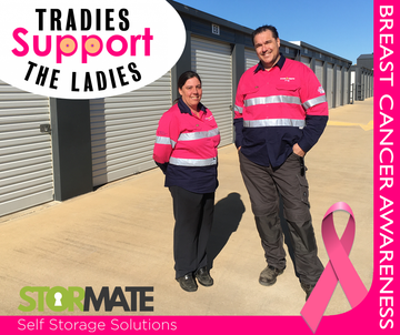A man and woman standing next to each other with a pink ribbon in front of a sign that says tradies support the ladies