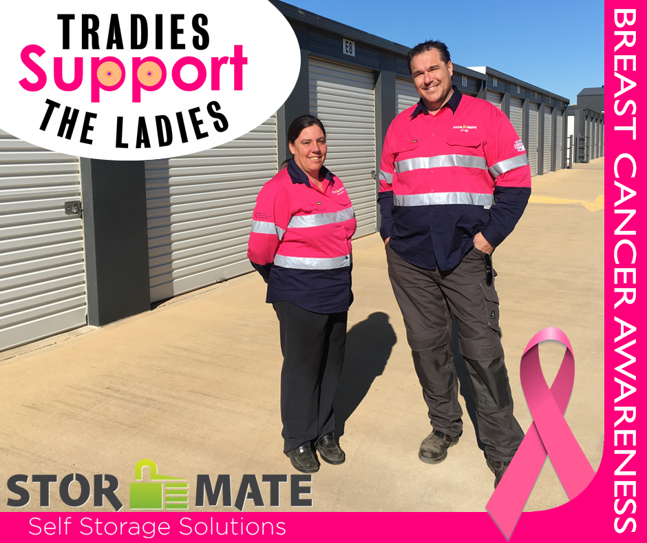 A man and woman standing next to each other with a pink ribbon in front of a sign that says tradies support the ladies