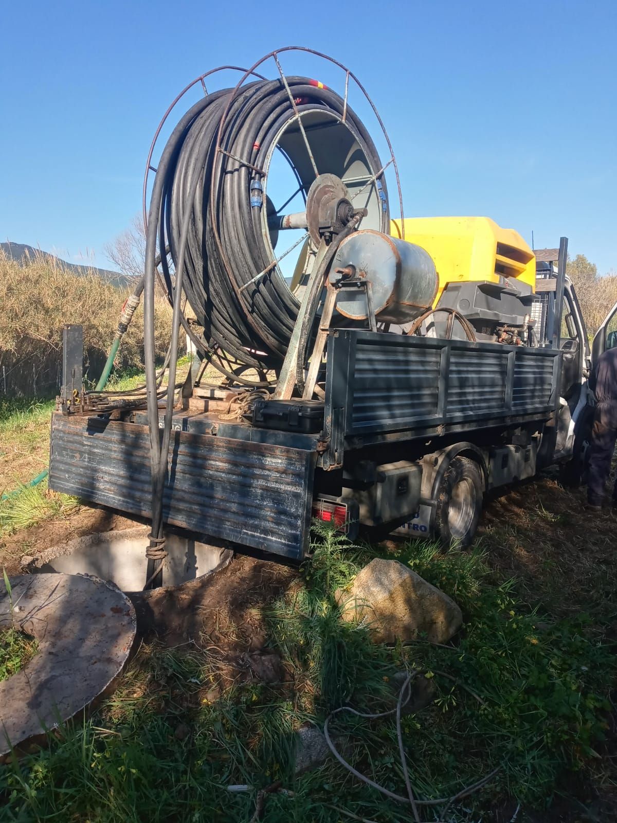 Camion con grande bobina di cavo nero e attrezzatura gialla, all'aperto, giornata di sole.