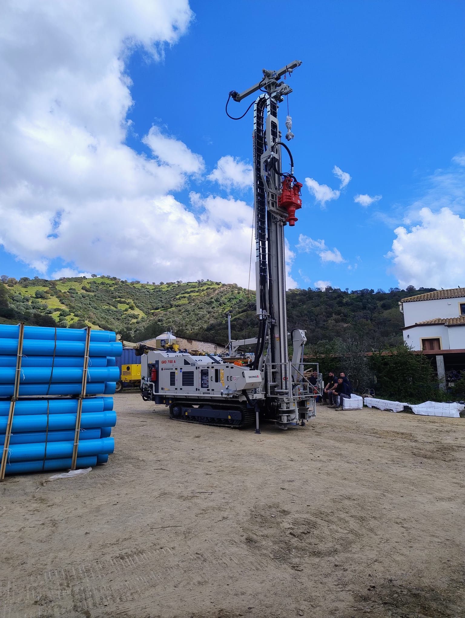 Piattaforma di perforazione in un cantiere. Tubi blu impilati. Colline verdi e cielo azzurro sullo sfondo.