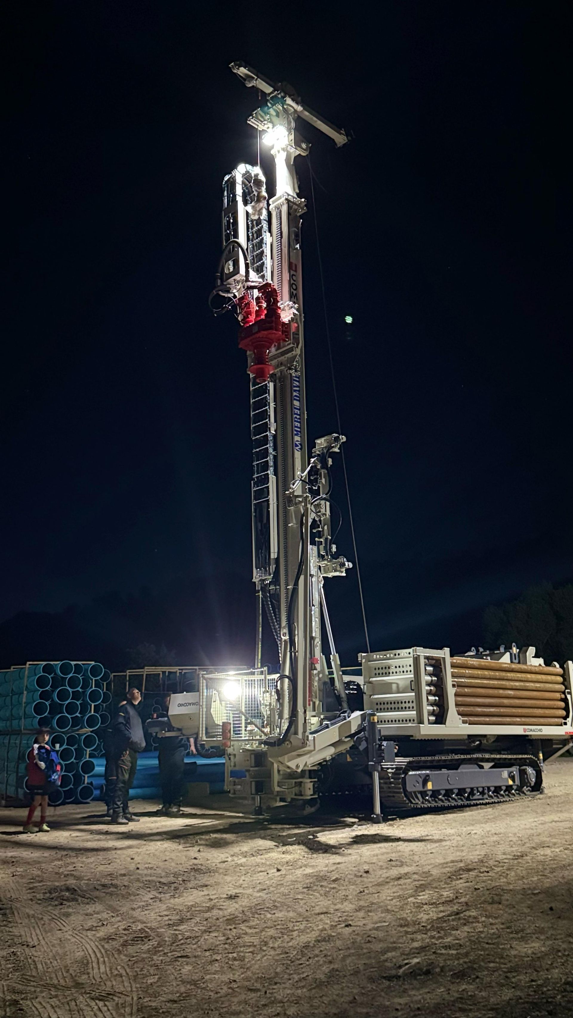 Piattaforma di perforazione di notte con luci intense. Persone in piedi nelle vicinanze in un cantiere edile.