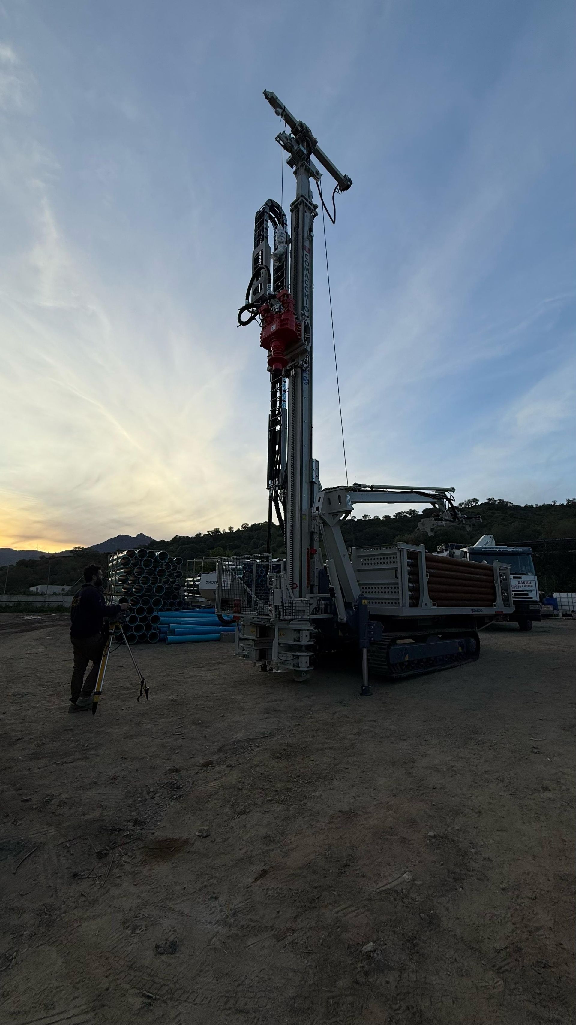 Piattaforma di perforazione in un cantiere. Una persona è in piedi nelle vicinanze. Cielo nuvoloso al tramonto.