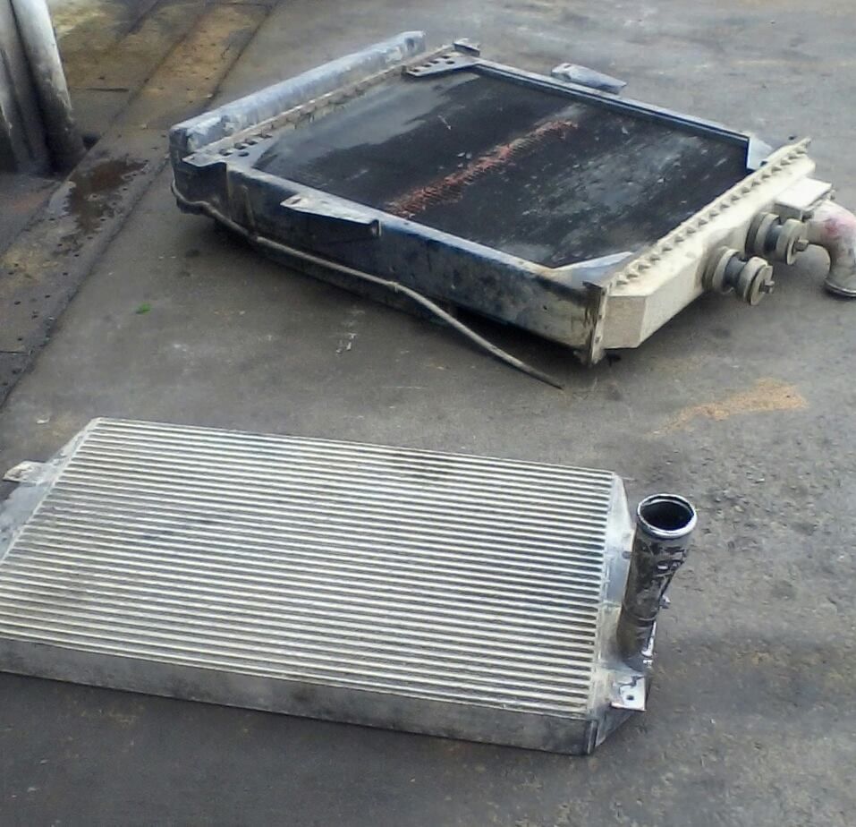 Two car radiators, one black, one silver, lying on a concrete surface.