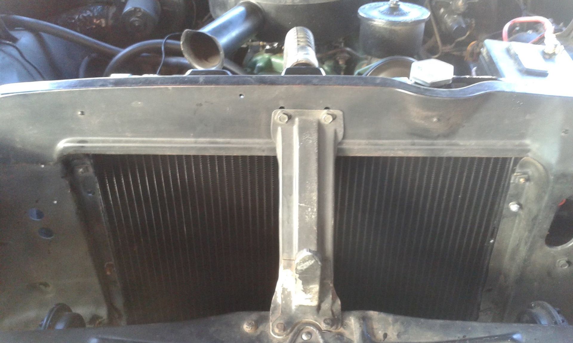 Car's front-end view of radiator with central support bracket, hoses, and engine components.