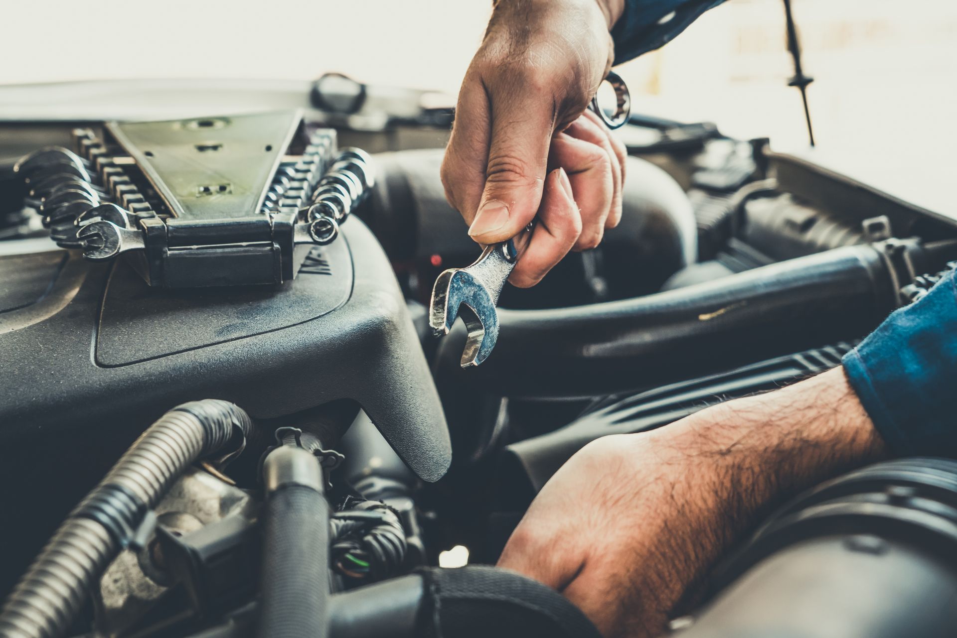 Hands holding a wrench, working on a car engine in an open engine bay.
